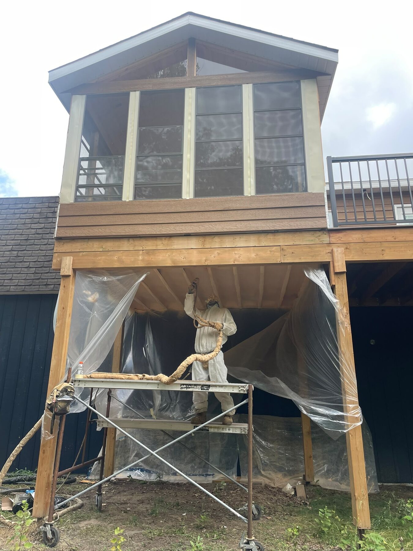Installer on scaffolding spray foaming the underside of a cantilevered second-floor sunroom addition