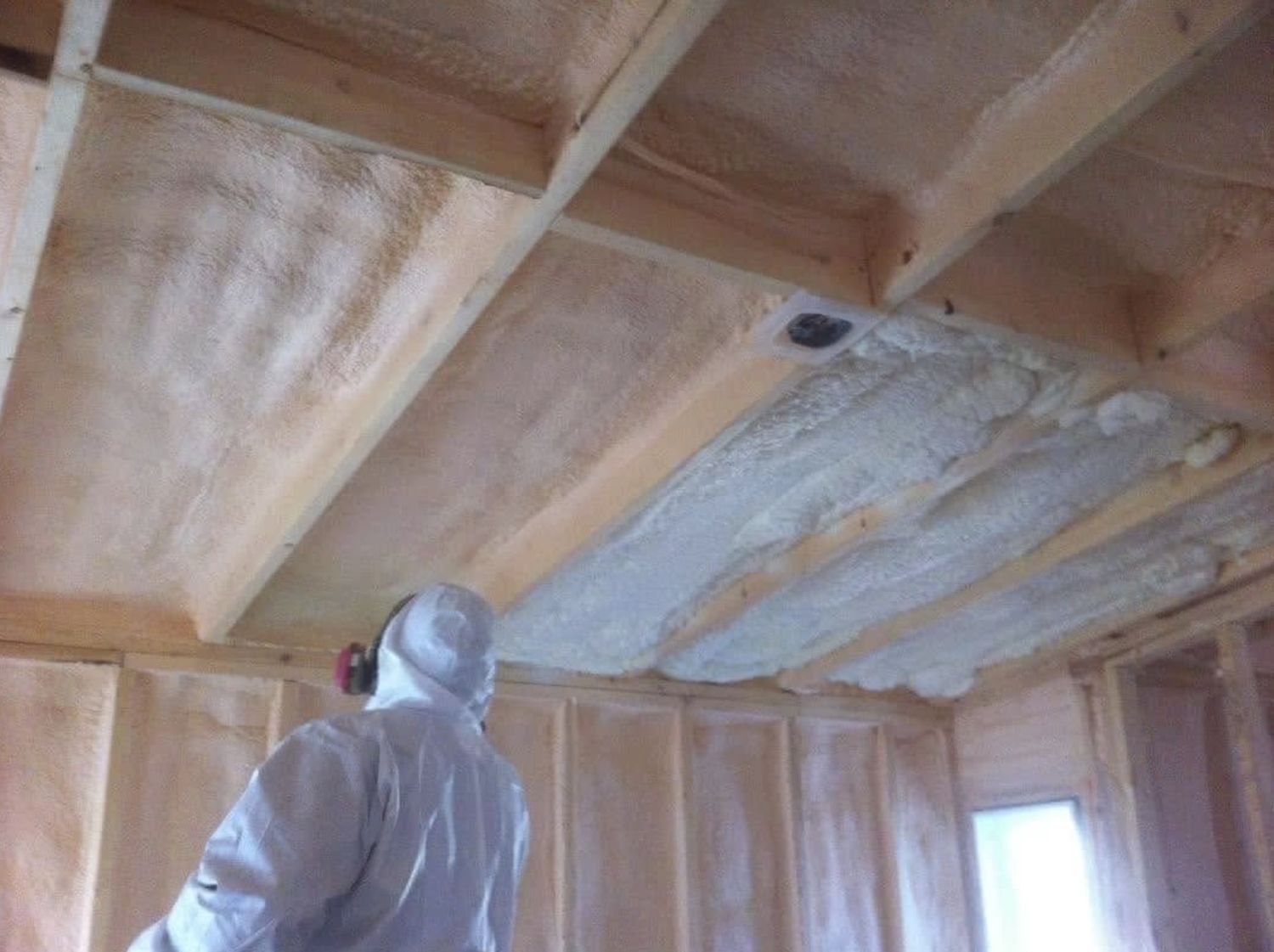 Ceiling joists with fresh spray foam being applied between them