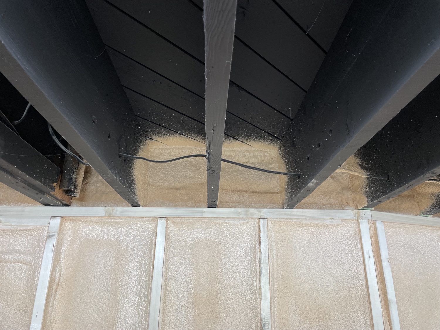 Cured closed-cell spray foam in a rim joist bay, uncoated, before the intumescent coating is applied