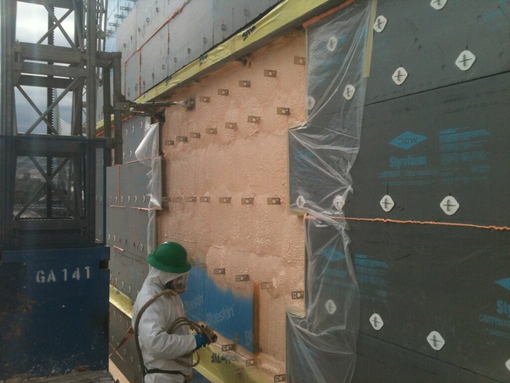 Ecologic installer in full PPE spray foaming a wall section next to Dow Styrofoam Cavitymate rigid insulation board