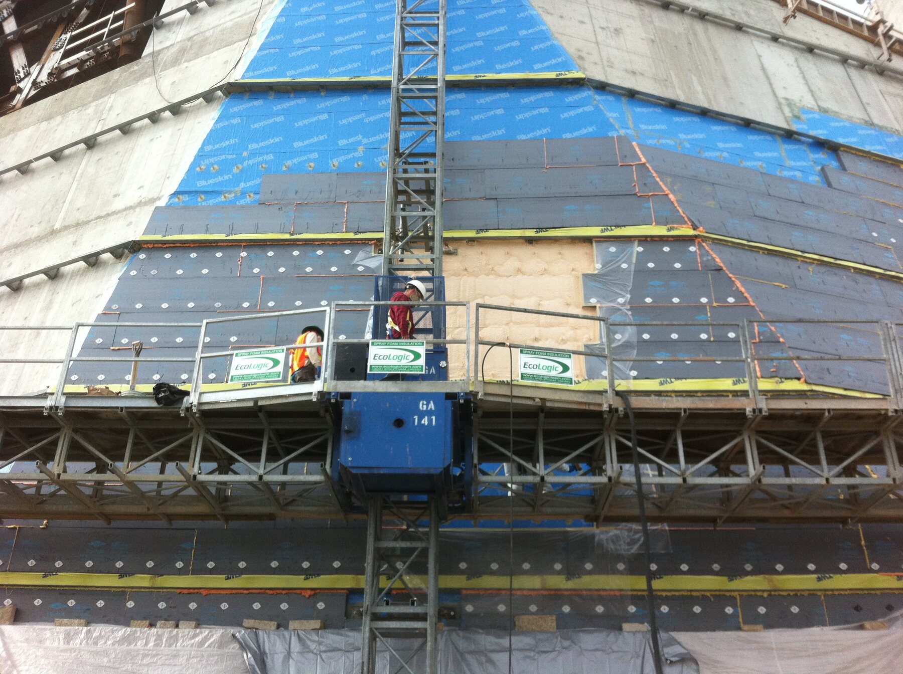 The Canadian Museum for Human Rights under construction, its distinctive angled glass and concrete tower visible with a hoist platform and Ecologic signage on the scaffold