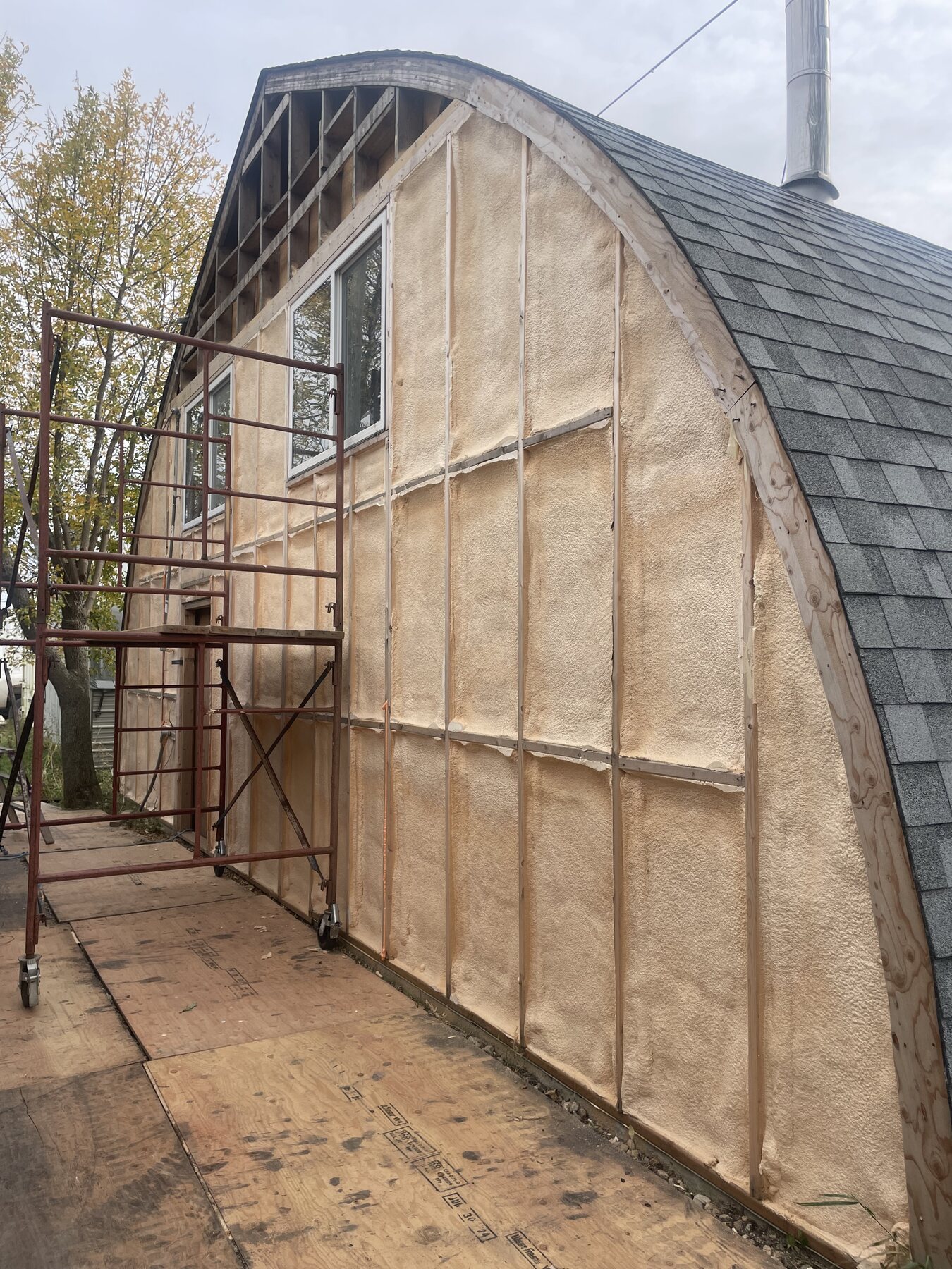 Exterior of an arch-roof quonset-style shop building mid-project, with scaffolding at the gable end