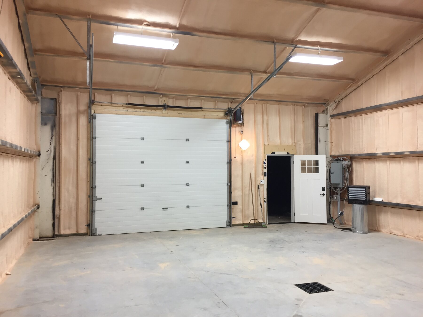 Finished steel shop interior with closed-cell spray foam on walls and ceiling, overhead door and man door