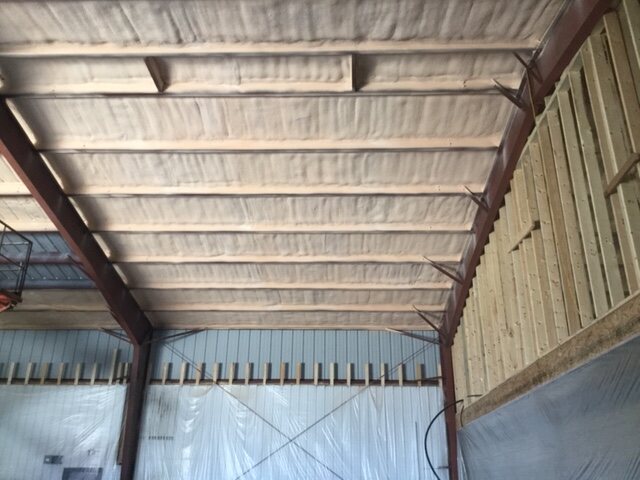Installer on a scissor lift spray foaming the underside of a steel shop roof deck